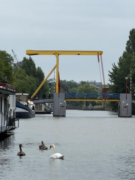 This serene photo captures a canal scene at Entrepotdok, Kadijken, Amsterdam, featuring a distinctive yellow drawbridge spanning the water